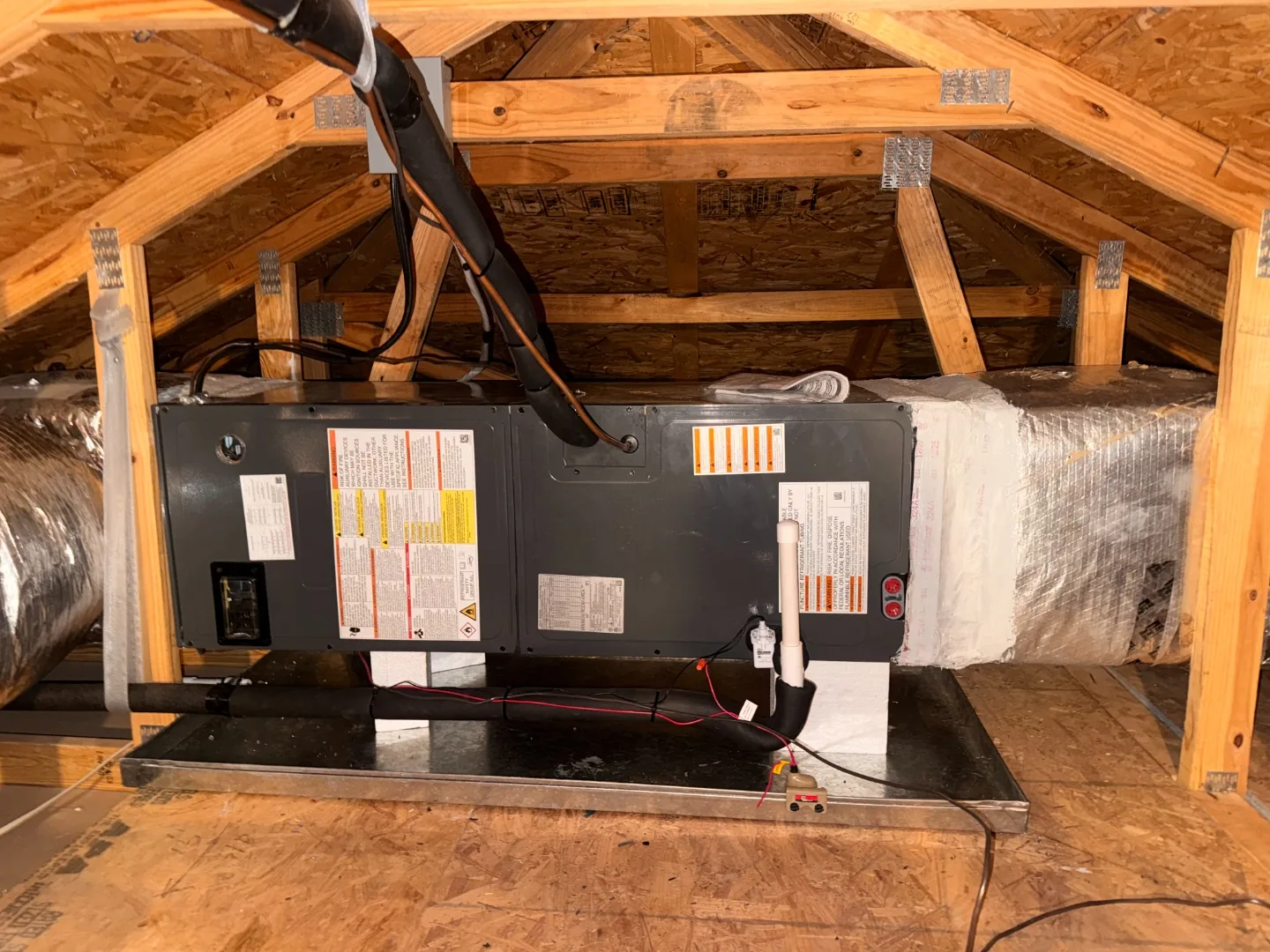 Air handler mounted on a metal platform in an attic, connected to insulated flexible ductwork among wood roof trusses